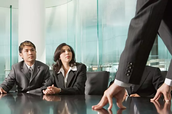Man en vrouw luisteren naar baas aan vergadertafel